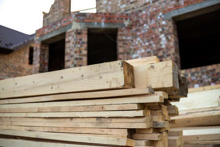 Close-up of piled stack of natural brown uneven rough wooden boards lit by bright sun. Industrial...