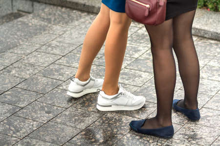 Two pairs of slim girls legs in short skirts, white leather sneakers and comfortable summer shoes on...