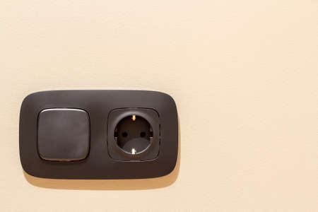 New gray electrical power outlet socket, plastic switch isolated installed on light yellow plastered...