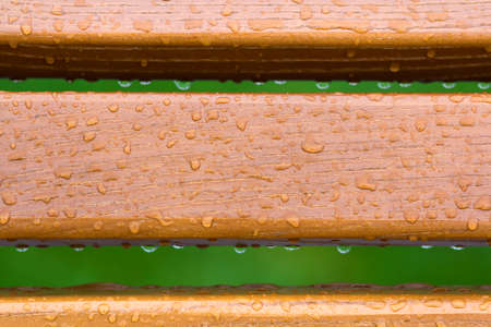 Wooden horizontal planks, boards, garden park bench back with transparent rain water drops on background of green fresh grass. Recreation and nature.の写真素材