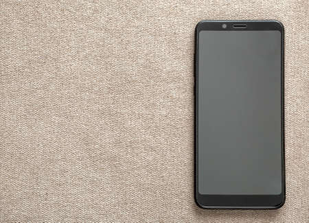 New black modern cellphone isolated on light cloth copy space background. Modern technology, communication and gadget design concept.の写真素材