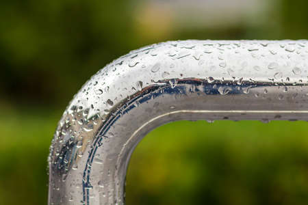Close-up of horizontal metal wet shiny pipe with big rain water drops on blurred abstract background.の写真素材