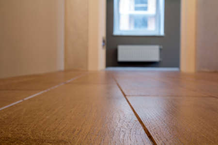 Spacious empty room, wooden floor light brown polished surface background in new apartment interior, beige walls, blurred glass window or door opening.の写真素材