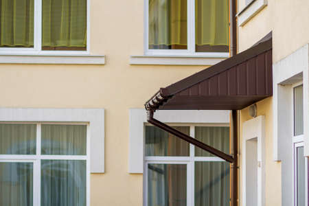 Building corner with new roof above entrance with steel gutter rain system. Durability, professional...