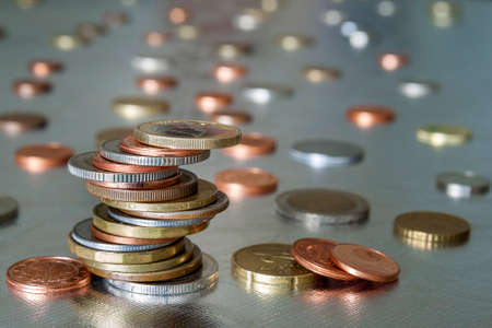 Pile of shiny coins different sizes and colors stacked unevenly on each other on colorful blurred...