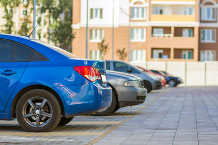 Side view detail of cars row parked in paved yard parking lot area on blurred building background on bright sunny day. Transportation and parking concept.の写真素材