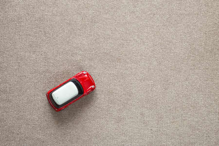 Top view of small bright red metal simple child toy car on light beige canvas cloth copy space...
