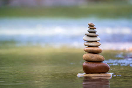 Close-up abstract image of wet rough natural brown uneven different sizes and forms stones balanced like pyramid pile landmark in shallow water on blurred blue-green misty copy space background.の写真素材