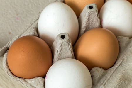 Hen eggs in open cardboard egg carton on kitchen table light copy space background. Healthy organic...