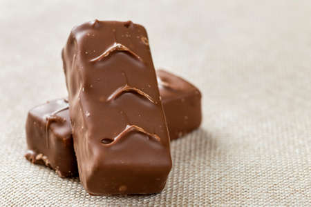 Two isolated isolated dark brown chocolate candy snickers bars on light canvas cloth copy space...