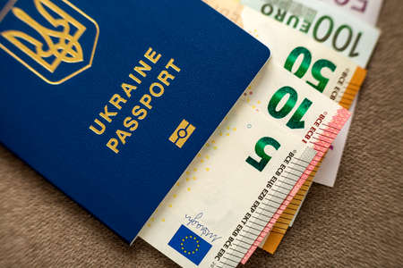 Ukrainian passport and money, American dollars banknotes bills on copy space background, top view. Traveling and  finance problems concept.の写真素材
