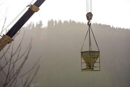 Bucket container with liquid concrete hanging on crane hook on copy space background. Construction...