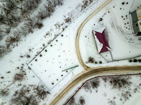 Aerial winter top view of house roof on fenced property, snowy field and dirty road.の写真素材