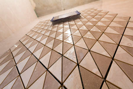 Unfinished reconstruction of bathroom or toilet with light beige geometric mosaic ceramic tiles installed on walls, place for lavatory and bath. Low angle, bottom view.の写真素材