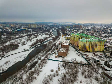 Aerial winter top view of modern developing city suburb area with tall buildings, parked cars and construction cranes. Urban cityscape on blue sky copy space background.の写真素材