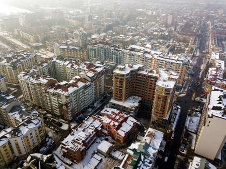 Aerial black and white winter top view of modern city center with tall buildings and parked cars on snowy streets.のeditorial素材