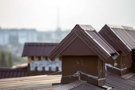 Close-up detail of new built brick plastered chimneys on house top with metal tile roof. Roofing,...