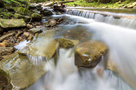 Fast flowing river stream with smooth silky water falling from big stones in beautiful waterfalls on...