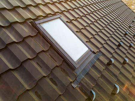 Close-up of new attic plastic window installed in shingled house roof. Professionally done building and construction work, roofing and installation concept.の写真素材