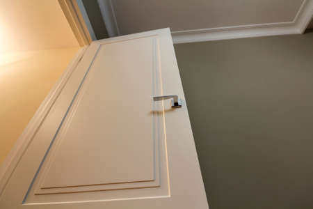 Apartment after renovation interior. White door with metal handle, light walls and ceiling, angle...