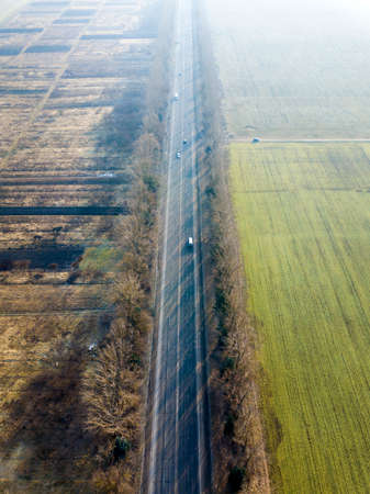 Aerial view of straight road with moving cars, trees and green fields on sunny day. Drone photography.の写真素材