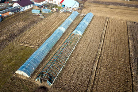Aerial view of long arched greenhouses covered with polyethylene in plowed spring field. Agriculture and farming.の写真素材