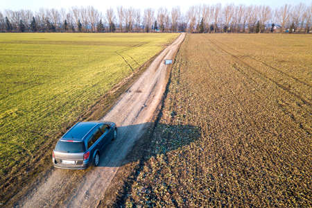 Aerial view of car driving by straight ground road through green fields on sunny blue sky copy space...