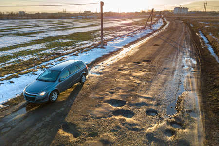 Aerial view of car moving along muddy rural road in bad condition on sunny spring or winter day.の写真素材