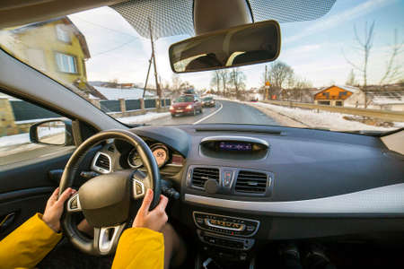Modern car interior with driver female hands on steering wheel, winter snowy landscape outside. Safe...