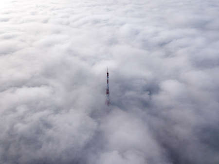 Aerial top view of foggy cloudy landscape with radio or TV antenna top on blue sky copy space...