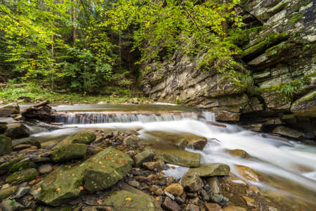 Fast flowing river stream with smooth silky water falling from big stones in beautiful waterfalls on...