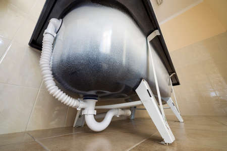 Bottom view of new ceramic bathtub on light bathroom tiles background. Installation and plumbing...