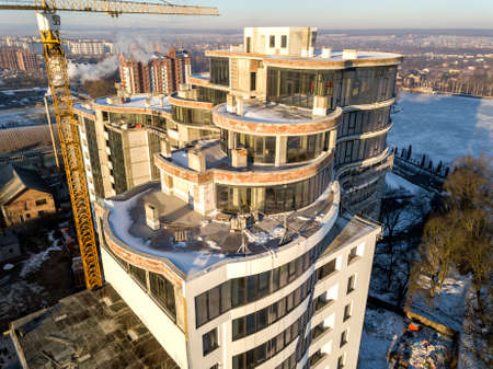 Aerial winter top view of modern developing city with tall apartment complex building under construction, parked cars, roofs and streets. Urban infrastructure, view from above.の写真素材