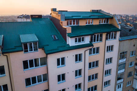Aerial view of attic annex room exterior with plastic windows, roof and walls covered with green metal siding planks, new gutter system on top of high multi-storey apartment building.の写真素材