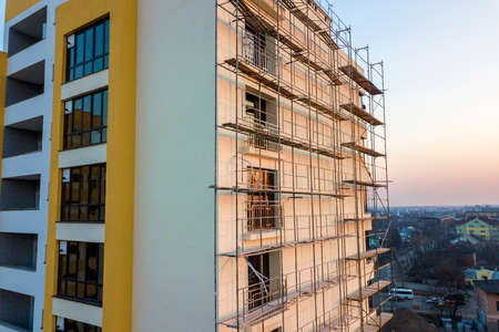 Apartment or office tall unfinished building under construction. Brick wall in scaffolding, shiny...