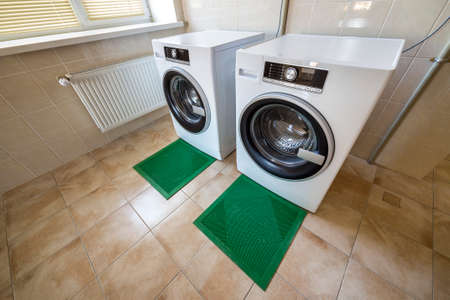 Modern new industrial washing machines in clean tiled bathroom or laundry room on rubber insulation mats.の写真素材