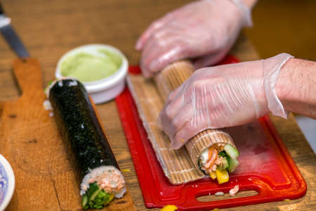 Process of making sushi and rolls. Close-up of man chef hands preparing traditional Japanese food at home or in restaurant on kitchen table.の写真素材