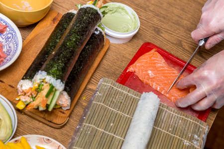 Process of making sushi and rolls. Close-up of man chef hands preparing traditional Japanese food at home or in restaurant on kitchen table.の写真素材