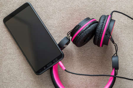 Headphone connected to cellphone isolated on light cloth flat copy space background. Modern...