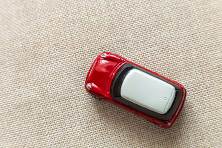 Top view of small bright red metal simple child toy car on light beige canvas cloth copy space...