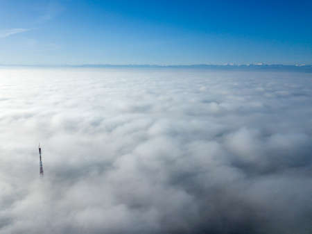 Aerial top view of foggy cloudy landscape with radio or TV antenna top on blue sky copy space...