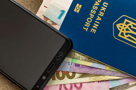 Modern black cellphone, money hryvnia banknotes bills and ukrainian travel passport on copy space...