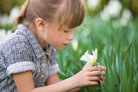 Cute pretty thoughtful child girl outdoor with white daffodil on sunny summer or spring day on blurred green background.の写真素材