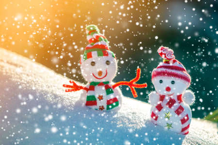 Two small funny toys baby snowman in knitted hats and scarves in deep snow outdoors on bright blue and white copy space background. Happy New Year and Merry Christmas greeting card.の写真素材