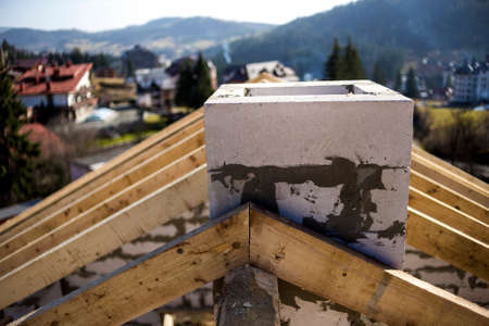 Close-up detail of roof frame of rough wooden lumber beams and chimney made of foam insulation blocks on blurred green background. Building, roofing, construction and renovation concept.の写真素材
