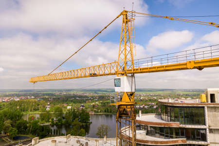 Apartment or office tall building under construction. Brick walls, glass windows, scaffolding and concrete support pillars. Tower crane on bright blue sky copy space background.の写真素材