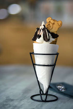 White plate with ice cream dessert in wafer cup with chocolate cookies and creative decoration...
