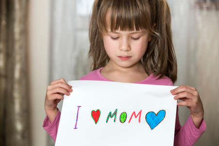 Cute child girl wit sheet of paper with colorful crayons painted words I love Mom. Art education, creativity concept.の写真素材