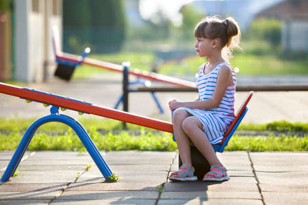 Cute young child girl outdoors on see-saw swing on sunny summer day.の写真素材