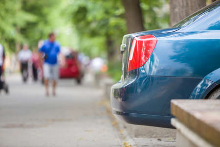 Car parked in pedestrian zone under trees on city street with walking people on summer day.